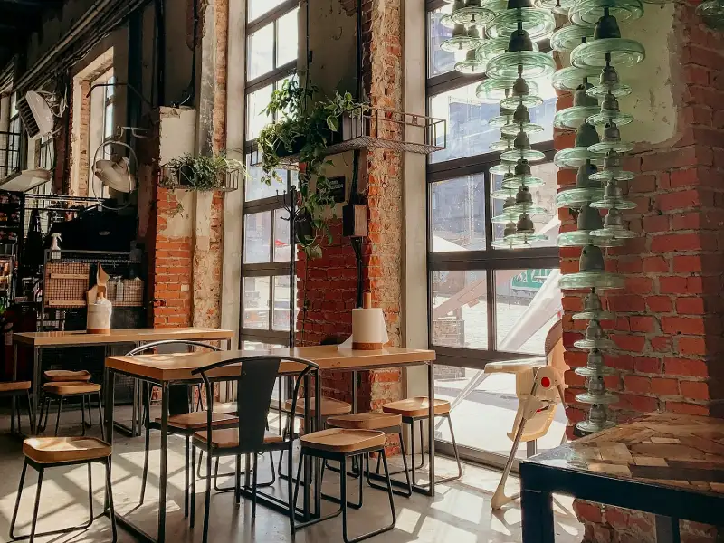Cafenea cu pereți de cărămidă, ferestre înalte și mese din lemn
